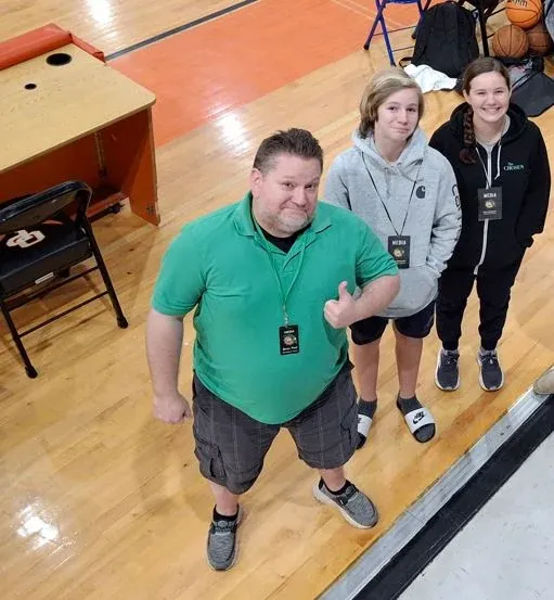 B.P., our on-air talent, courtside at a basketball game, giving a thumbs up beside two young members of the media crew